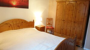 Ein Schlafzimmer mit einem Holzbett, einem Nachttisch mit Lampe, einem Holzschrank und einem Stuhl.
