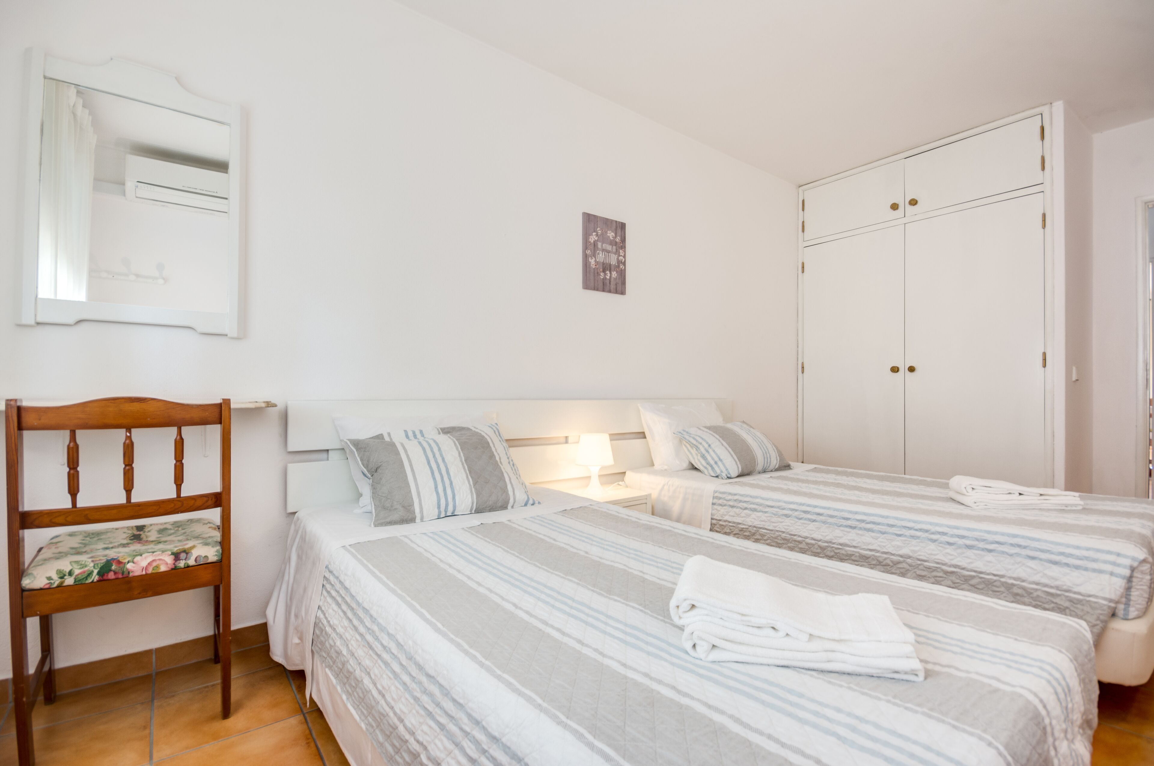A bedroom with two beds, a wooden chair, a mirror, and a wardrobe.