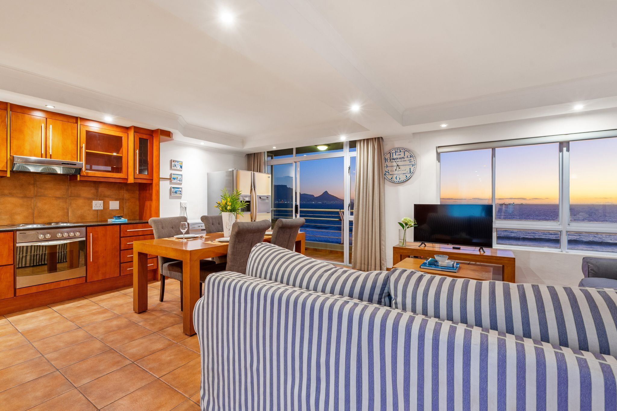 A modern living room with a sofa, TV, dining area, kitchen, and large windows with a city view.