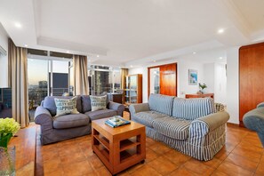 A modern living room with a sofa, a striped sofa, a coffee table, and a view of the city through large windows. - Ocean View 701 (Cape Town)