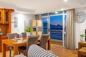 A modern hotel room with a dining area, a kitchen, and a balcony with a city view.