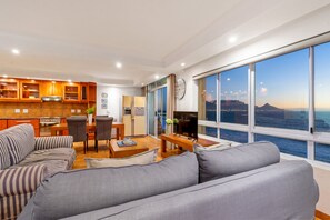 En moderne stue med et stort vindue, en sofa, et spisebord og et køkkenområde.
