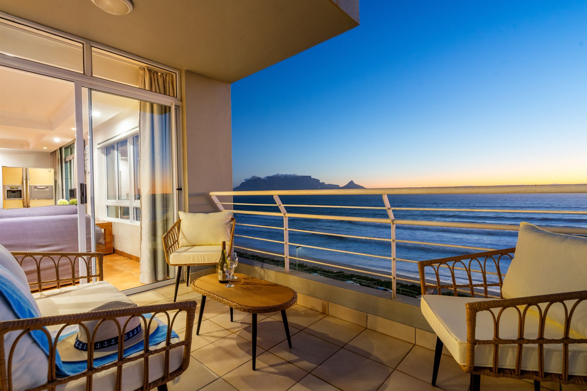 Varanda com vista para o mar, uma cama e uma mesa com uma garrafa.