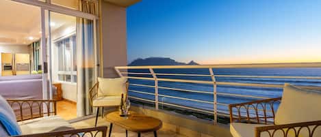 Varanda com vista para o mar, uma cama e uma mesa com uma garrafa.