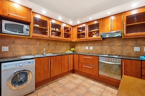 A kitchen with wooden cabinets, a microwave, a washing machine, and a stove. - Ocean View 701 (Cape Town)