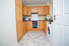 A compact kitchen with wooden cabinets, a microwave, an oven, and a washing machine.