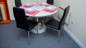 Un tavolo rotondo da pranzo con quattro sedie nere, piatti bianchi e tovagliette rosse.