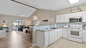 Una cocina moderna con armarios blancos, una isla central y un comedor con sofá gris.