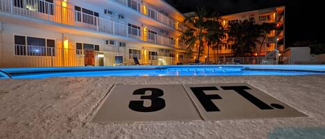 Hotel com piscina, placa indicando a profundidade da piscina e um edifício com várias andares e varandas.