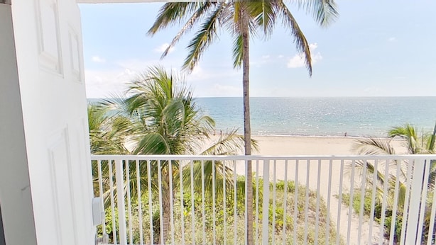 A balcony with a view of a beach, palm trees, and the ocean. - Full Remodel, Direct Beachfront 3rd Floor Corner Unit, Fantastic Views! (Pompano Beach)