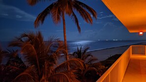 Une vue nocturne d’une plage bordée de palmiers et d’un bâtiment à la façade orange.