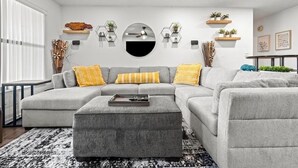Una sala de estar moderna con un sofá seccional gris, una mesita de centro y estantes decorativos en la pared.