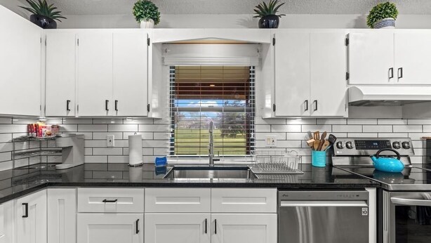 Una cocina moderna con armarios blancos, un lavavajillas de acero inoxidable y un hervidor azul.