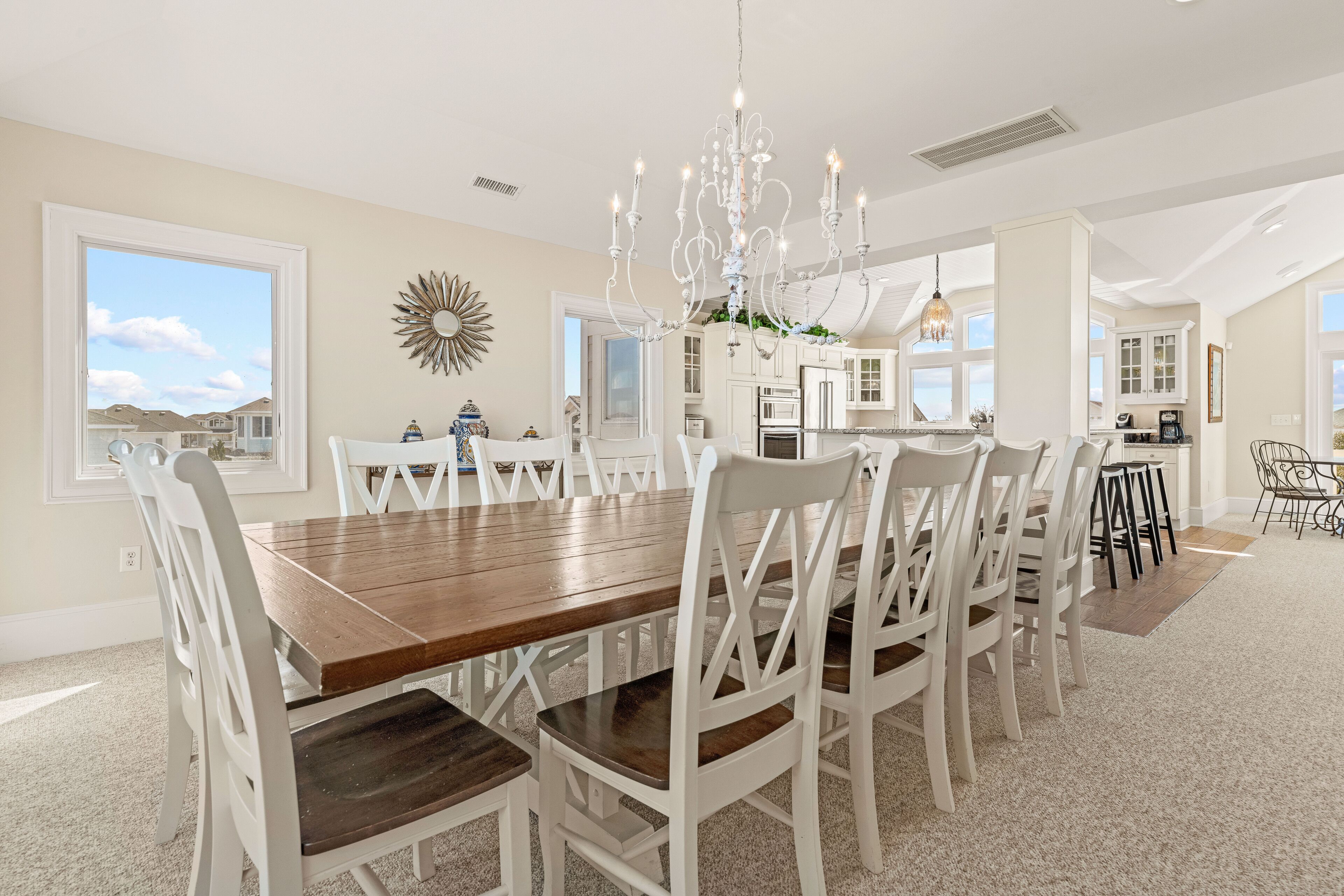Une salle à manger spacieuse, avec une grande table en bois et des chaises blanches, un lustre, et une vue sur les montagnes grâce à de grandes fenêtres.