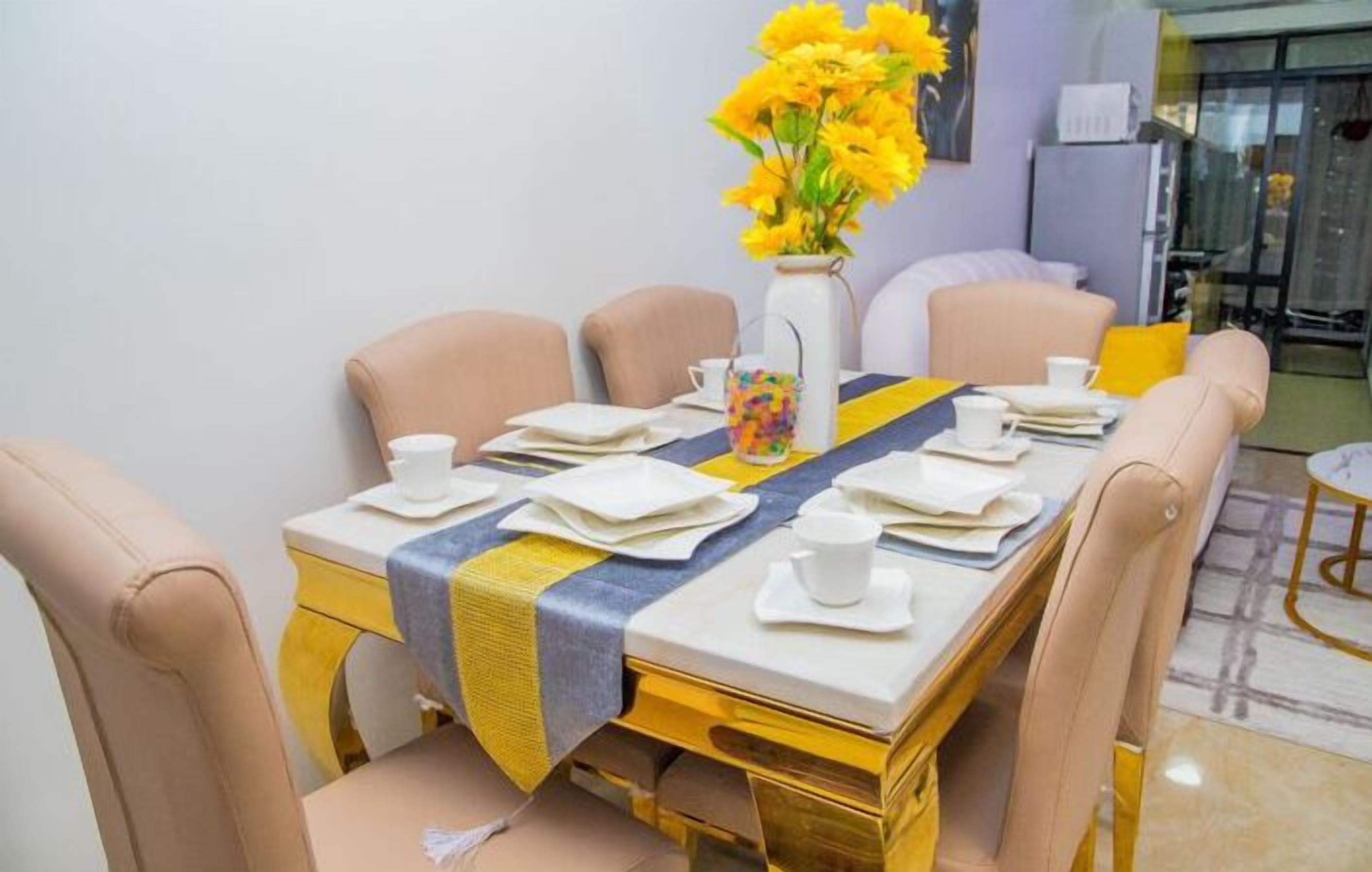 A dining area with a table set for four, a vase of yellow flowers, and a yellow-striped table runner.