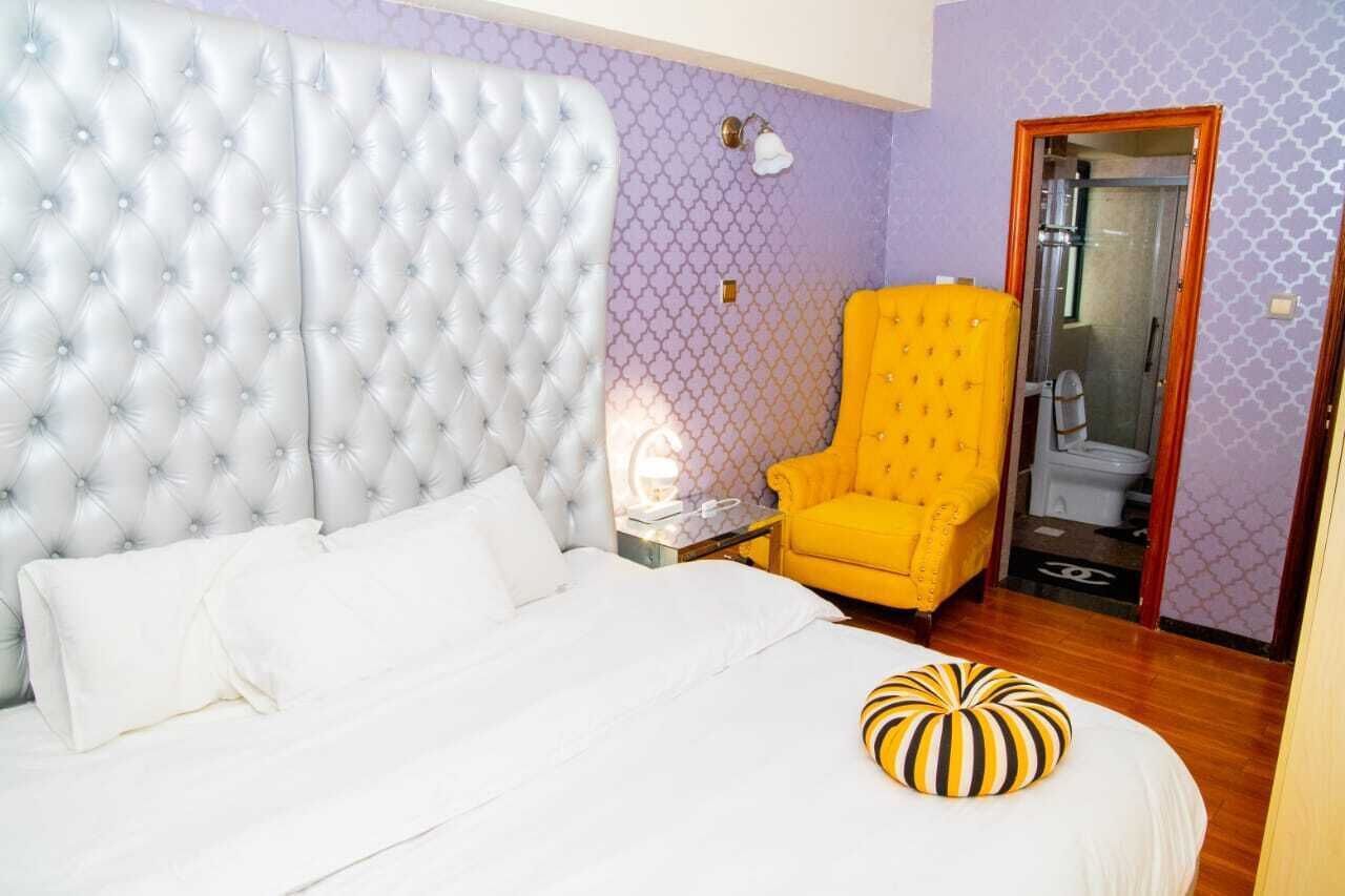 A bedroom with a tufted headboard, a white bed, a yellow armchair, and a striped pillow.