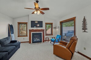 A living room with a fireplace, a ceiling fan, a television, and a large window.