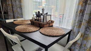 Une table à manger avec des sets de table en fibres tressées, des chaises blanches et un panier contenant des couverts.