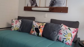 Un lit avec une couette et des oreillers aux motifs floraux dans des tons turquoise, une tête de lit en bois et deux reproductions d’œuvres d’art représentant des animaux, encadrées et accrochées au mur.