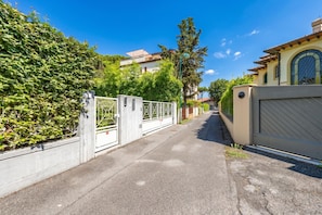 A residential street with a gated entrance, a hedge, and a building with a tiled roof. - Terrazza Apuana A Few Steps From The Sea (Forte dei Marmi)