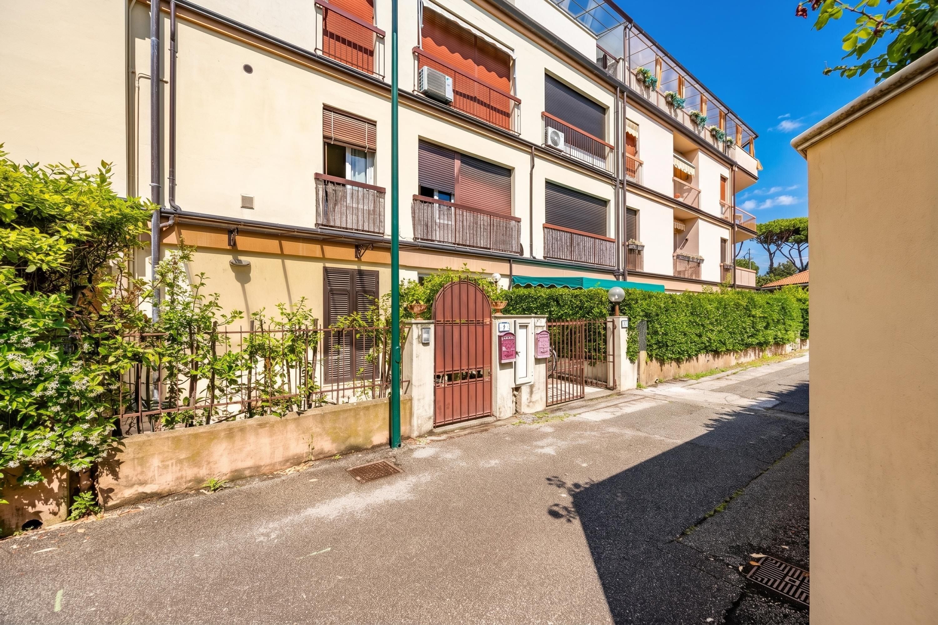 Um edifício residencial com várias andares, varandas, entrada com portão e céu claro.
