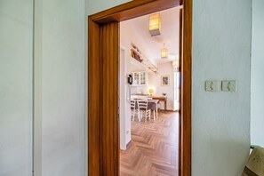 A hallway leading to a dining area with a herringbone floor, wooden door frame, and a white wall with two light switches.