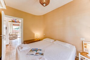 A hotel room with a bed, a nightstand, a lamp, a chair, a door leading to a balcony, and a shelf with books. - Terrazza Apuana A Few Steps From The Sea (Forte dei Marmi)