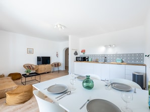 Une cuisine moderne avec des meubles blancs, un pare-feu noir et blanc, et un coin repas avec une table blanche dressée pour deux personnes.