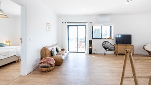 Un vaste espace de vie comprenant un canapé, un pouf et un téléviseur posé sur un meuble.