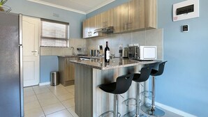 A modern kitchen with a central island, bar stools, a built-in microwave, and a wine bottle. - Ocean Breeze 59 (Cape Town)