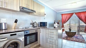 A modern kitchen with a Bosch washing machine, an oven, and a coffee maker. - Ocean Breeze 59 (Cape Town)