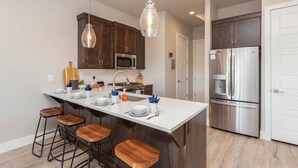 A modern kitchen with a central island, stainless steel appliances, and wooden bar stools.