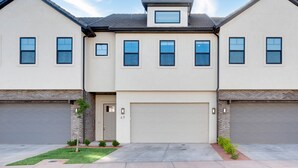 A two-story residential building with a garage, a small front yard, and a clear sky.