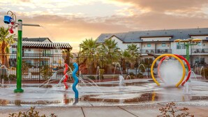 A water park with a fountain, a twisting sculpture, and a building in the background.