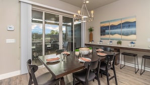 A dining area with a large table set for six, surrounded by chairs, with a view of a deck and outdoor area through glass doors. - Oasis at Ocotillo 48, Private Pool and Spa! Ping Pong table, Nintendo Switch & Resort pool (Santa Clara)