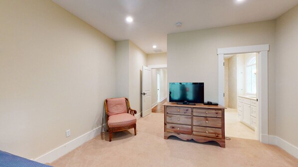 A room with beige walls, a wooden dresser, a pink chair, and a television. - Large Golf Course View Home with Large Private Pool and Spa! (Hilton Head)