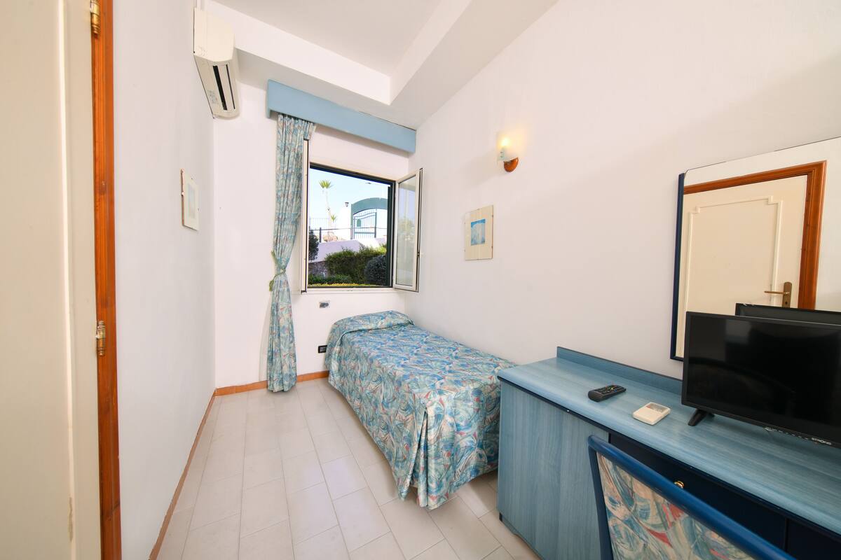 A small, tidy room with a bed, a TV, and a window with curtains.