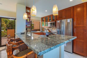 A kitchen with a granite countertop, stainless steel appliances, wooden cabinets, and a dining area with wicker chairs.