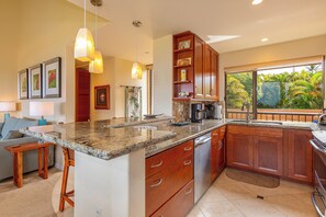 Una cocina moderna con encimeras de granito, armarios de madera y un amplio ventanal con vistas a un jardín.