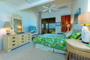 A bedroom with a bed, a dresser, a desk, a ceiling fan, and a window with a view.