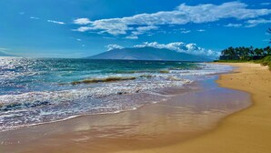 A beach with clear blue water, a sandy shore, and a mountain in the background.