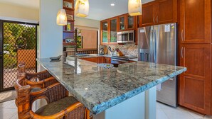 A kitchen with granite countertops, stainless steel appliances, wooden cabinets, and a dining area with wicker chairs.
