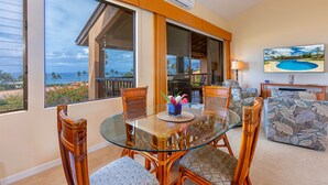 A dining area with a glass table and wicker chairs, overlooking a scenic view of the ocean.
