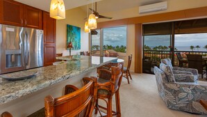 A modern kitchen with a large island, wooden bar stools, and a view of the ocean.