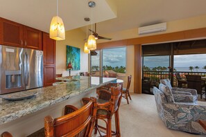 A modern kitchen with a large island, wooden bar stools, and a view of the ocean.
