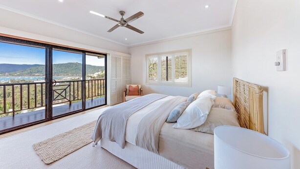 Quarto com cama grande, ventoinha no teto, vista por uma porta de correr e varanda.