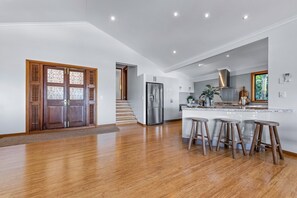 A modern kitchen with a central island, stainless steel appliances, and wooden stools. - Coral Sea Views (Airlie Beach)