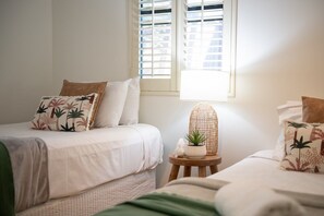 A bedroom with two beds, a window with blinds, a bedside lamp, and a small table with a plant. - Coral Sea Views (Airlie Beach)