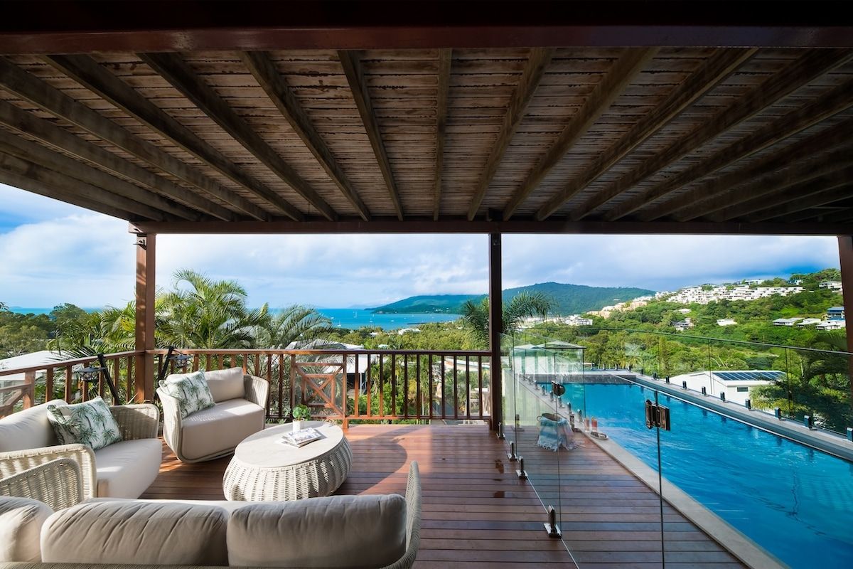 A covered outdoor area with a pool, wicker furniture, and a view of the landscape.