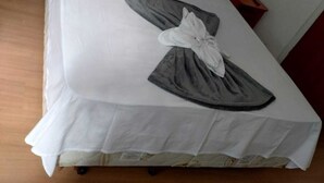 A neatly made bed with white linens, a gray towel, and a white pillow. - Mônaco Hotel (Juiz de Fora)